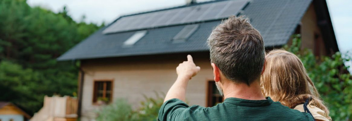 Eine Person zeigt auf ein Hausdach mit Photovoltaik-Anlage